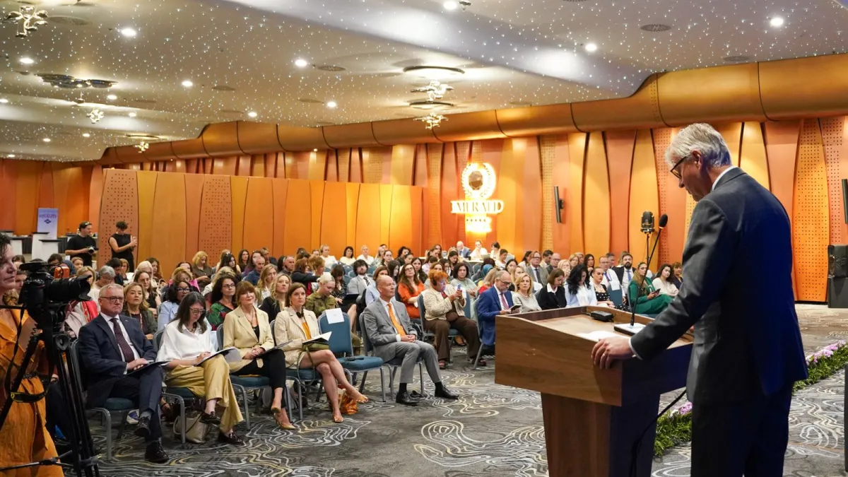 Men speaking at a podium, in front of an audience 
