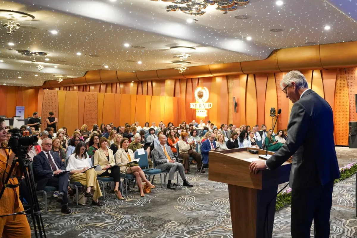 Men speaking at a podium, in front of an audience 
