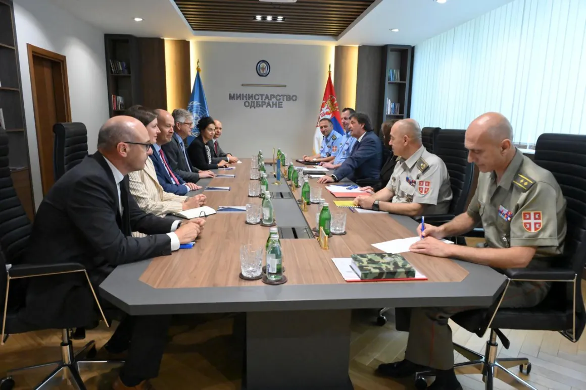 Official men and women in civilian and uniform sitting at a round table 