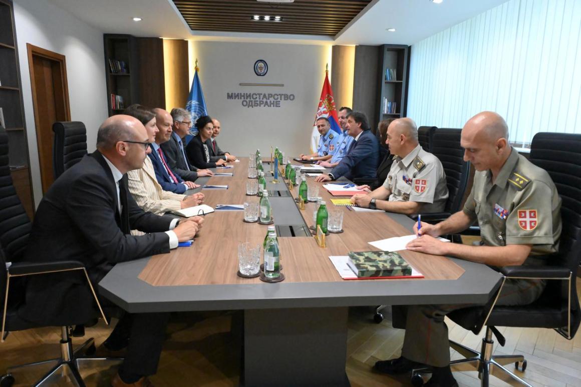 Official men and women in civilian and uniform sitting at a round table 